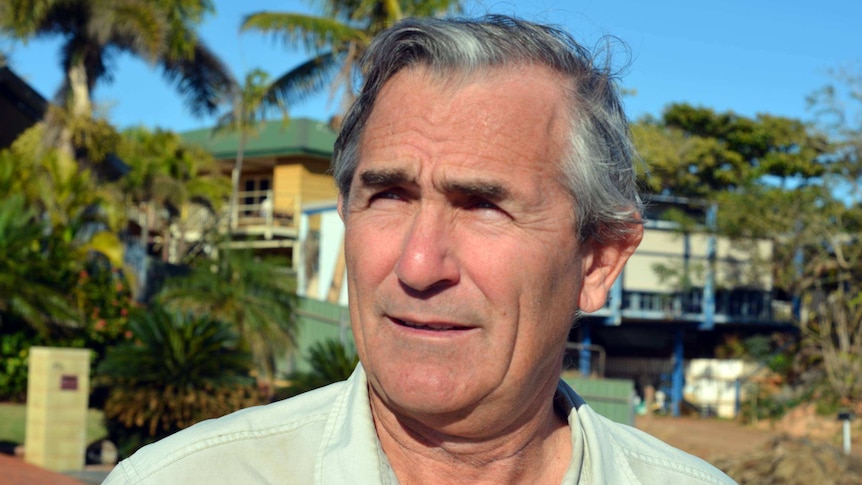 A close-up image of a man wearing a light green shirt with greying hair.