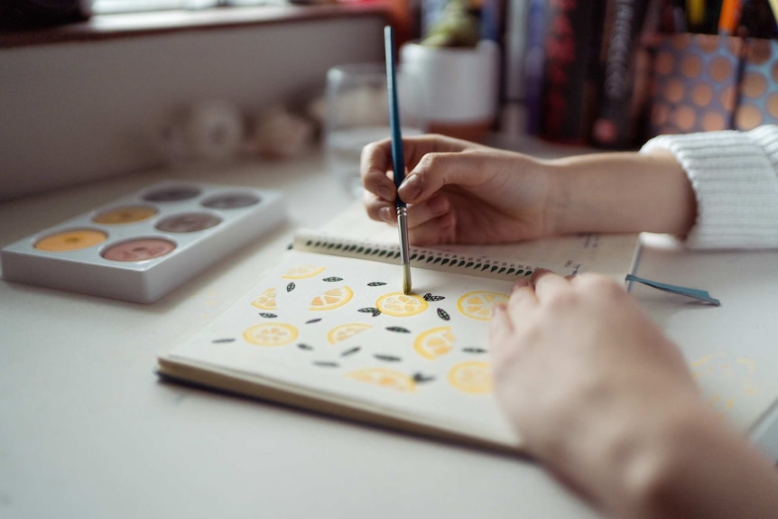 A woman uses a paintbrush to colour patterns in a notepad