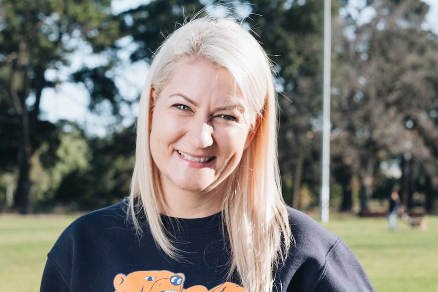 Angela is holding a sherrin football in her left arm and smiling.