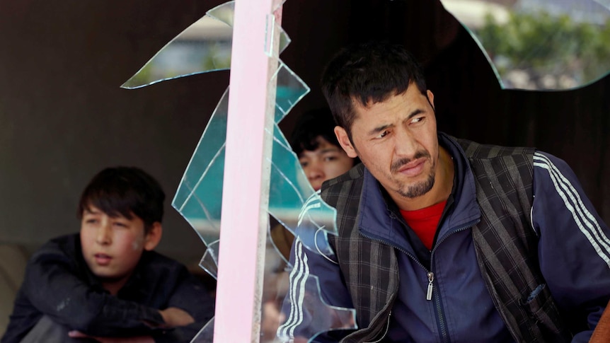 A man and two boys are seen looking out through a broken window at the site of the suicide attack.