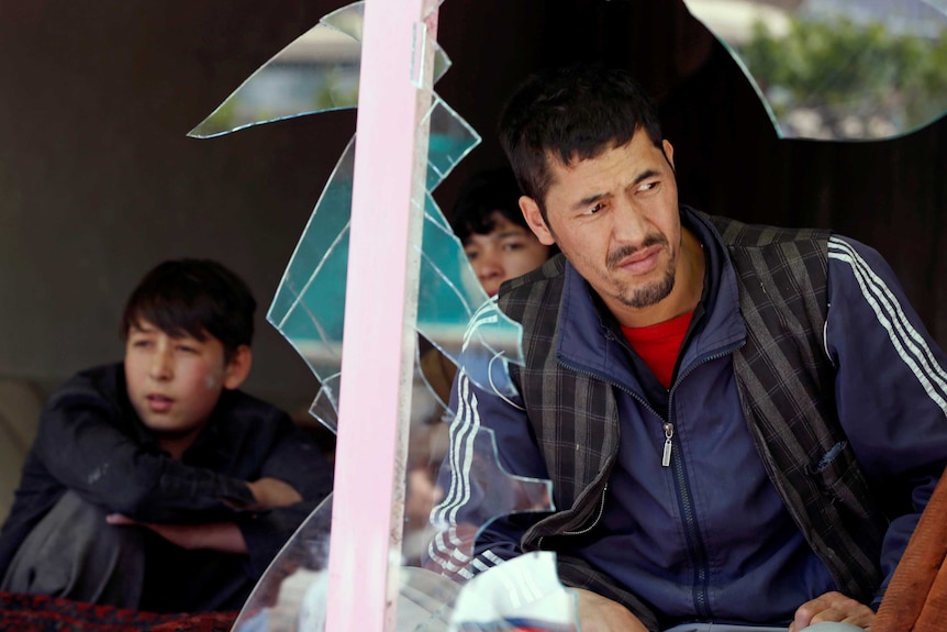 A man and two boys are seen looking out through a broken window at the site of the suicide attack.