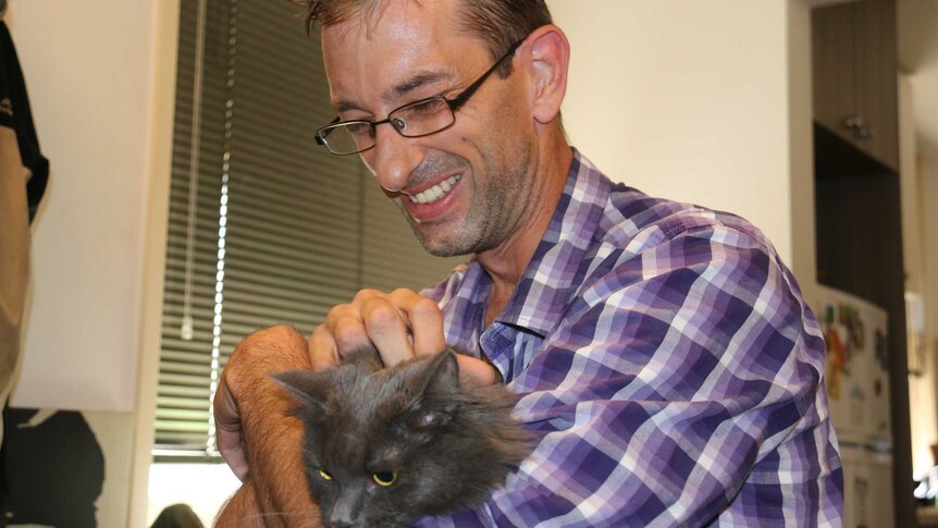 David Alberti smiles while patting his cat.