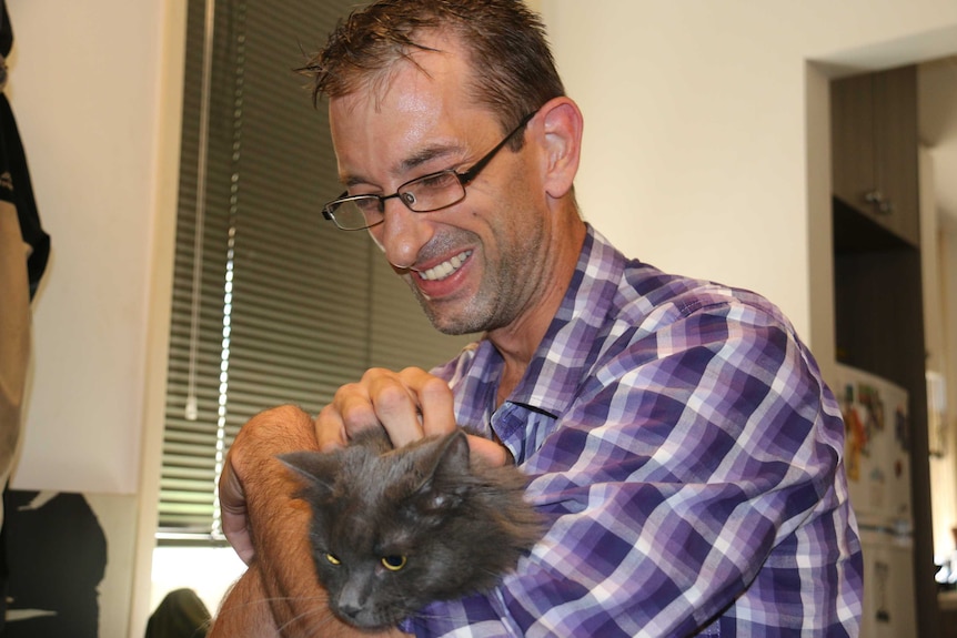 David Alberti smiles while patting his cat.