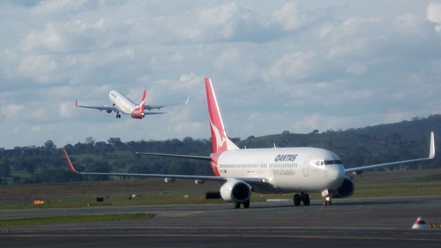 A Qantas plane can be seen taking off as another taxis along the runway.