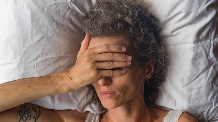 Woman in bed with hand over eyes