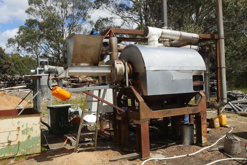 a complicated machine made of rusty tubing and stainless steel sits in the yard of a sawmill