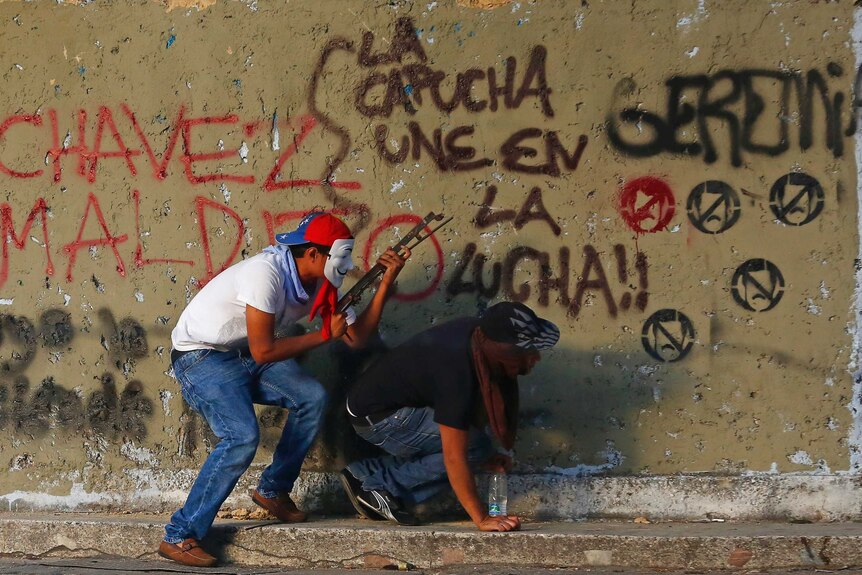 Protestors take shelter behind a wall covered in graffiti