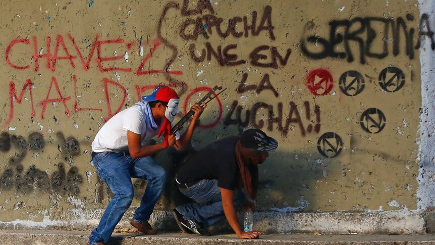 Protestors take shelter behind a wall covered in graffiti