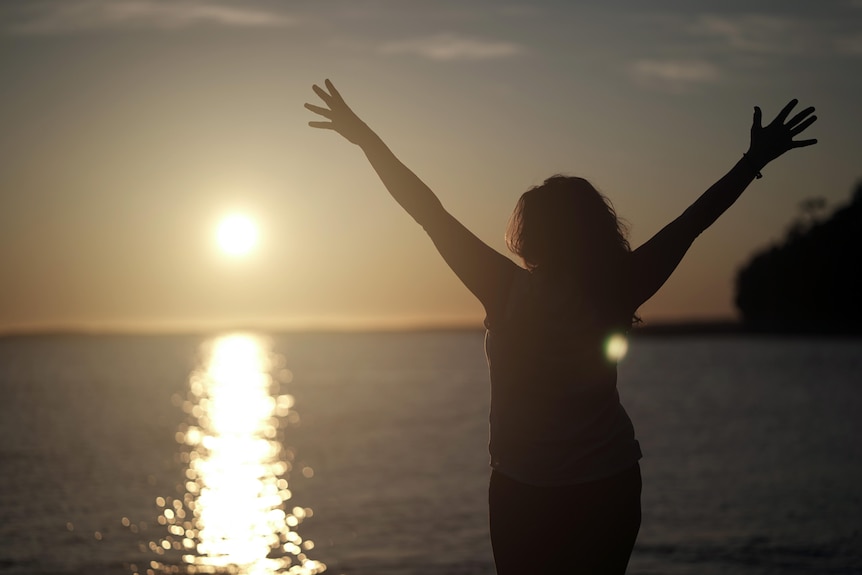 Woman in silhouette stands at Jervis Bay with her arms outstretched