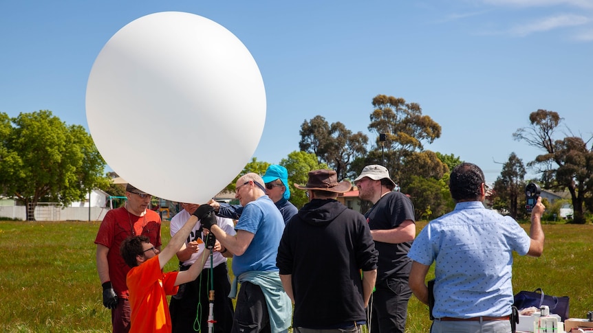 Several men with science instruments stand around a big white balloon
