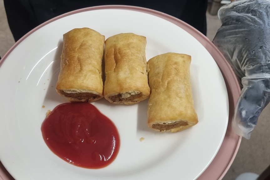 Three mini sausage rolls on a plate with tomato sauce.