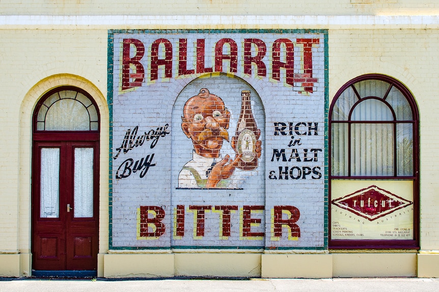 Drawn sign of cartoon barman with a bottle of Ballarat Bitter beer.