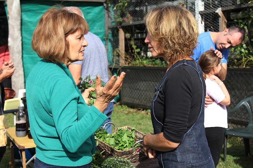 Two women facing each other while they swap herbs from rattan baskets at a food swap west of Brisbane.