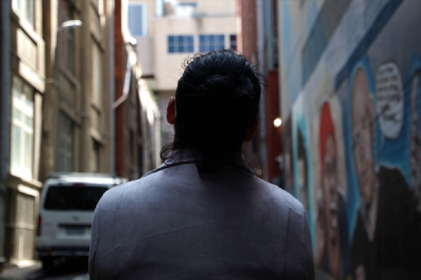 A picture looking down the a Melbourne laneway, with graffiti on one side and the back of a woman in the front of the picture.