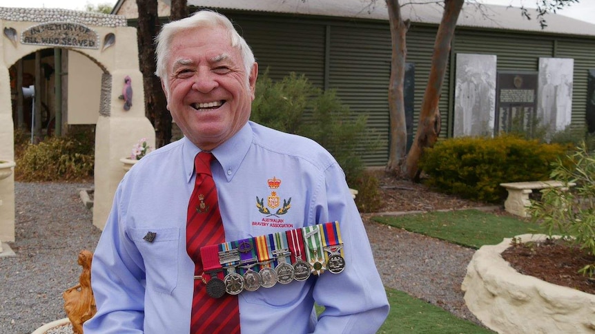 A man wearing military medals stands in front of a museum.