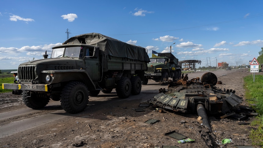 Ukrainian army vehicles drive past the remains of a Russian tank