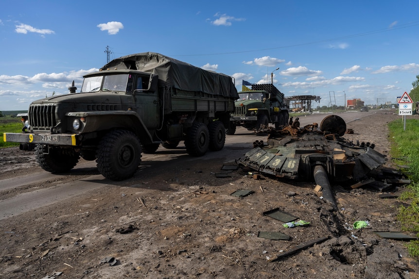 Ukrainian army vehicles drive past the remains of a Russian tank