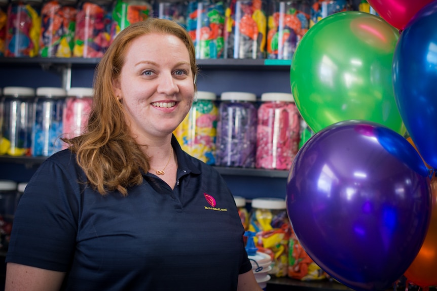 A woman stands in front of jars full of latex balloons while holding a bunch of inflated balloons.