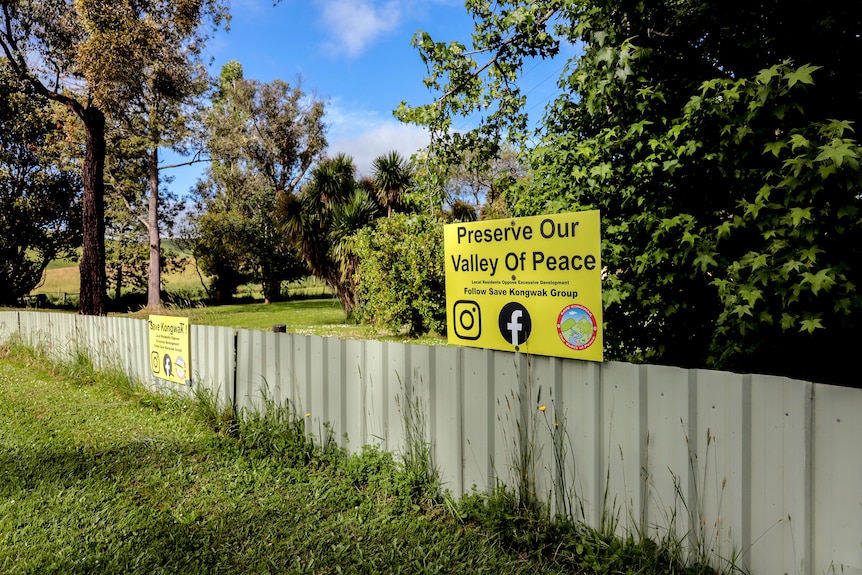 A yellow sign reading Preserve our Valley of Peace displayed on a fence with trees and grass in background
