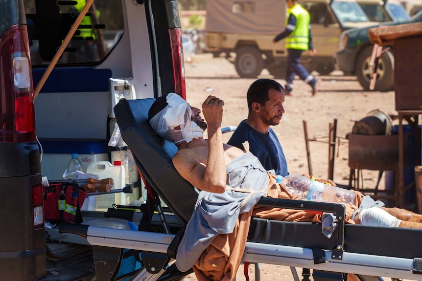 A man on a stretcher with a bandage on his head, with another man sitting next to him