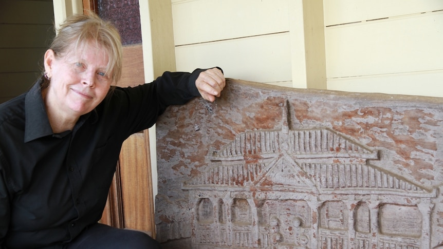 A woman wearing a black jumper crouching next to a wood carving.
