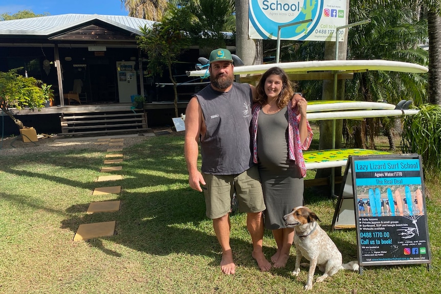 A man with his arm around a woman standing in front of surfboards