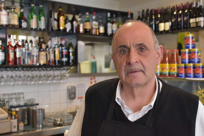 Mario De Pasquale stands in front of shelves stacked with liquor and tomato paste.