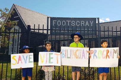 Five students hold signs saying "save Viet bilingual program heart FPS" as they stand in front of their school.