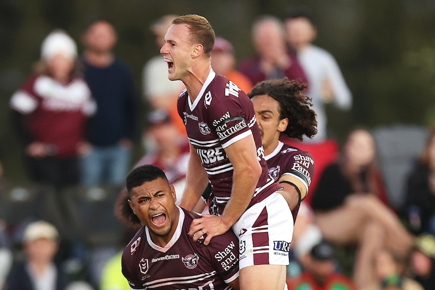 Daly Cherry-Evans and Morgan Harper jump on the back of Manly Sea Eagles teammate Haumole Olakau'atu after an NRL try.