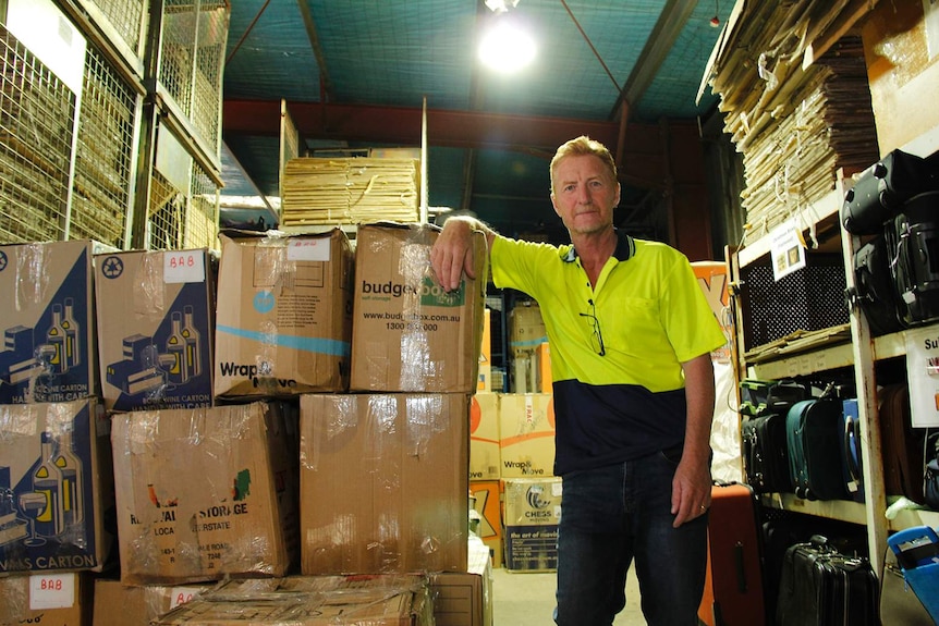 A man in a high-vis polo shirt leans on a stack of boxes in a warehouse.