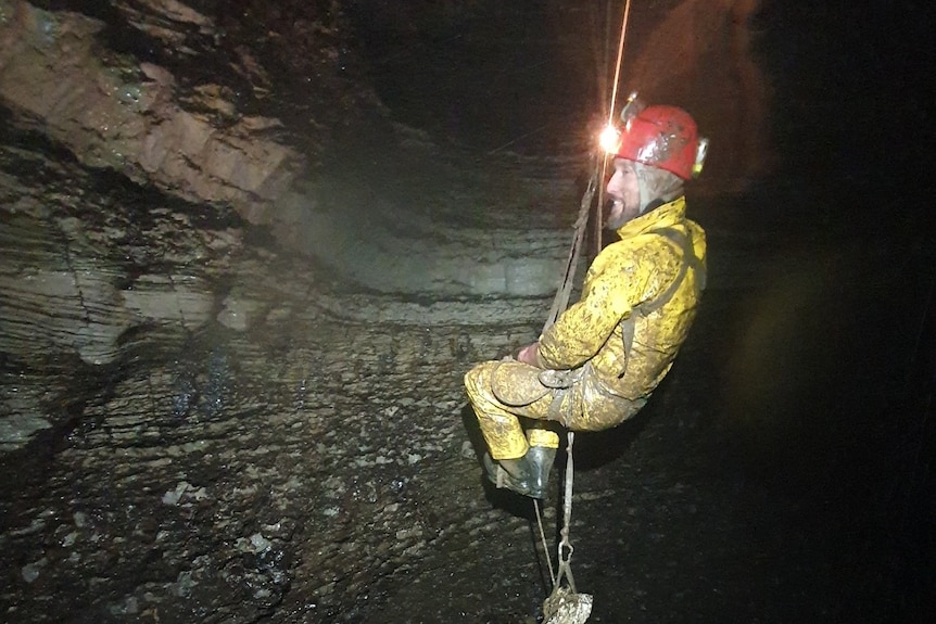 A man abseils down into a dark abyss.