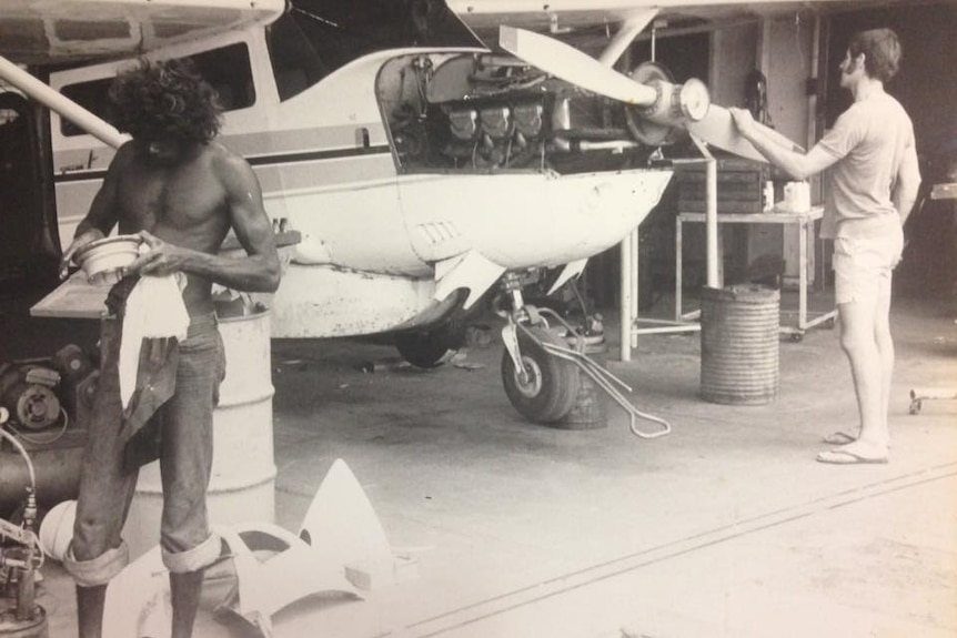 A black and white picture of two men, one of them a young Yingiya Guyula, working at the MAF hangar.