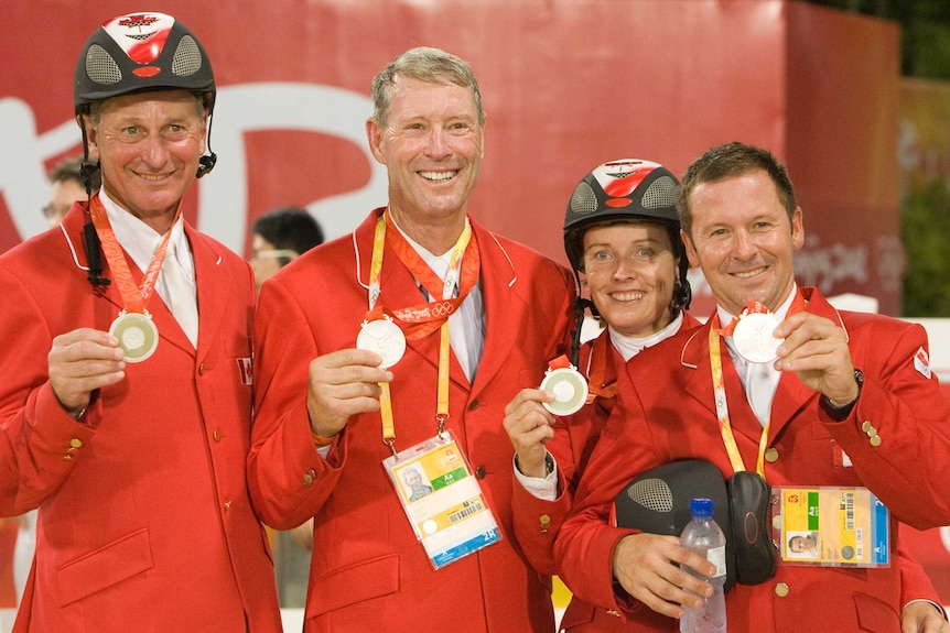 A team of showjumping riders smile with their Olympic silver medals.