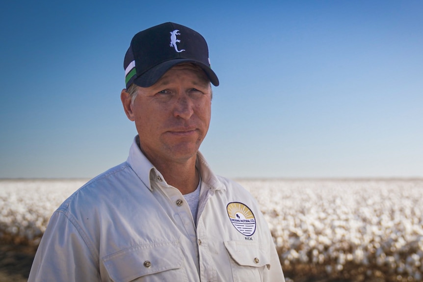 Image of a man wearing a cap with a cotton farm behind him.