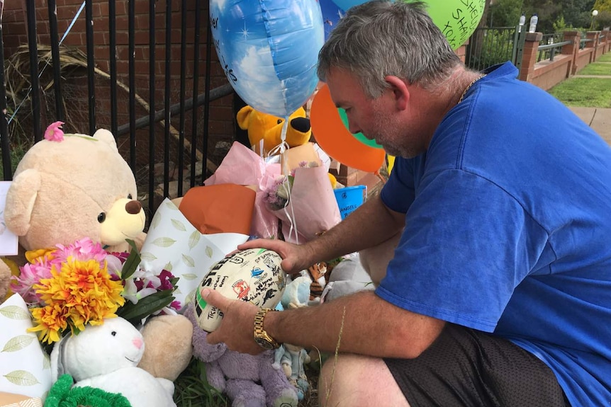 Joseph Shorey holds a football among other tributes left for his two sons at the scene of the crash.