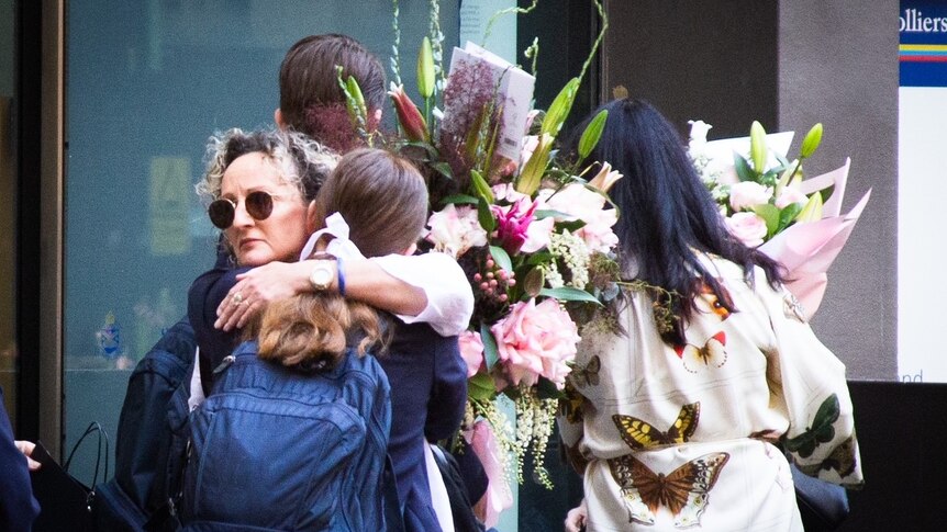 a woman embraces a student as flowers are placed outside of St Andrews Cathedral school