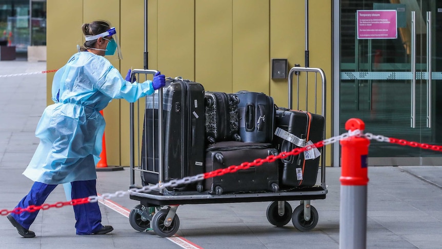 A Hotel quarantine staff member is seen wearing full PPE gear while pushing a luggage trolley.