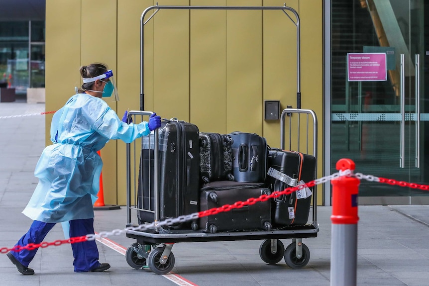 A Hotel quarantine staff member is seen wearing full PPE gear while pushing a luggage trolley.