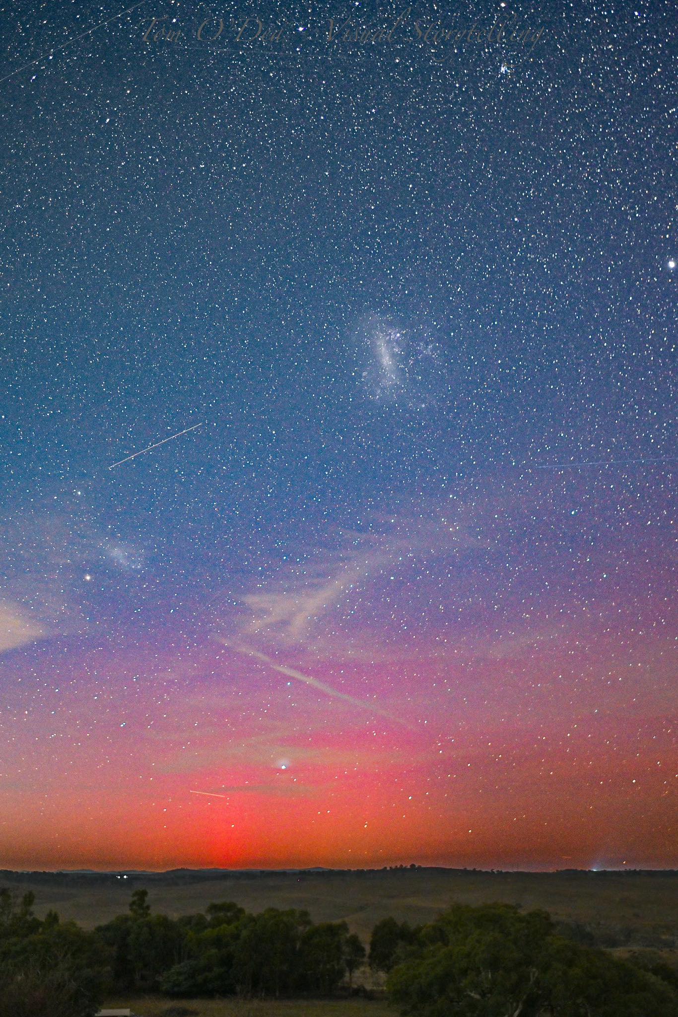 A pink and orange light is visible over the horizon in the night sky over Yass farmland