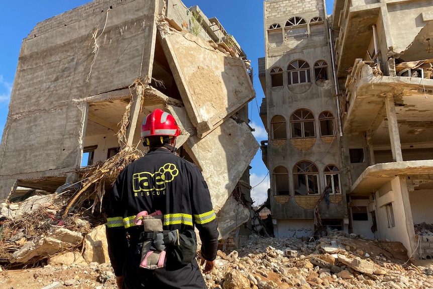 Rescuer in red hard hat stands before a mountain of crumpled  buildings 