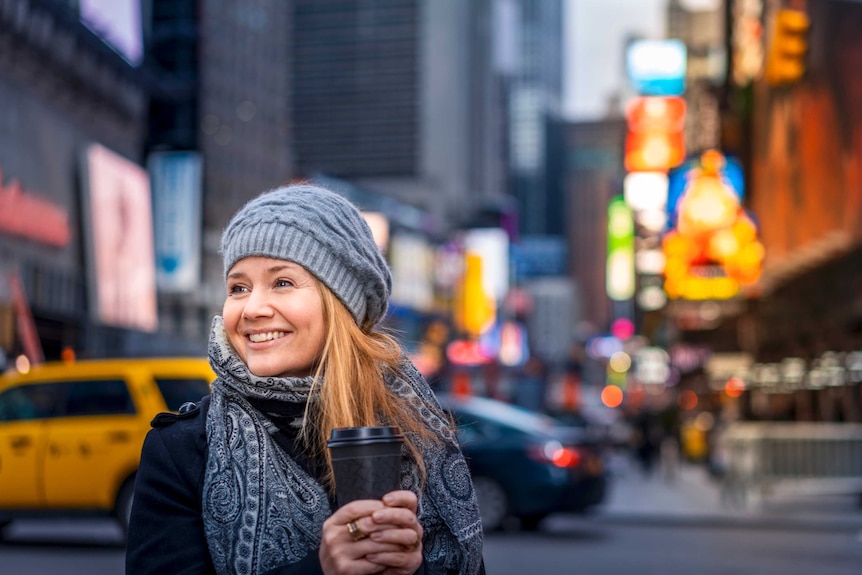 Woman holding coffee smiles facing left of frame.