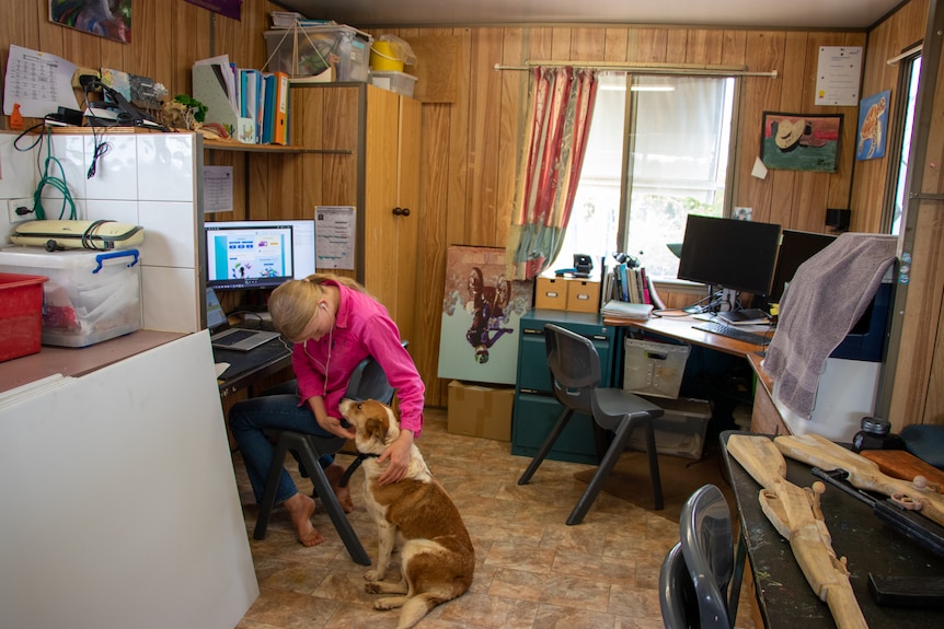 Lucy Faggotter pats her dog while sitting at her school desk on her station north of Longreach, November 2022.