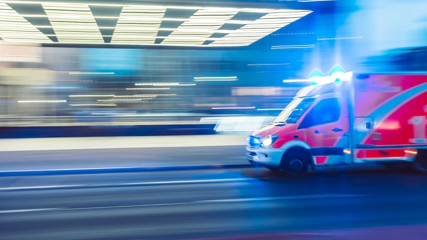 An ambulance speeds along a road with lights and sirens on