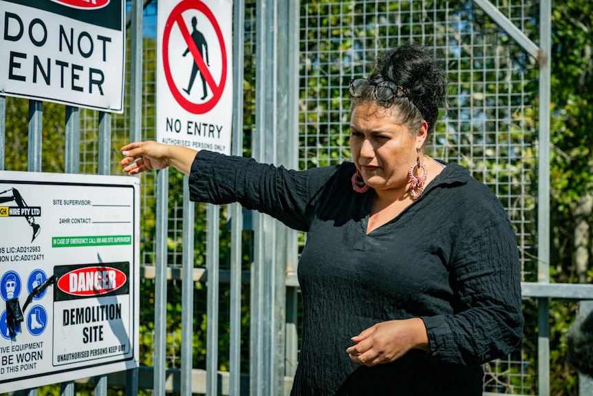 An Aboriginal woman  wearing a black long-sleeved t-shirt stands in front of a gate that says 'no entry'