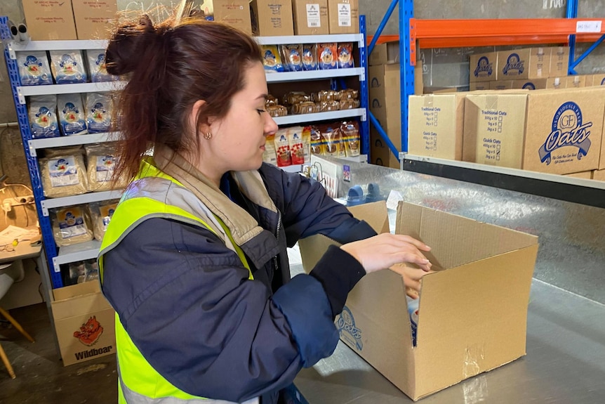 A lady packing a box with packets of oats. 