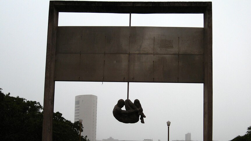 A stone sculpture of a curled man hanging from an arch commemorating the victims of Torture under Brazil's military dictatorship