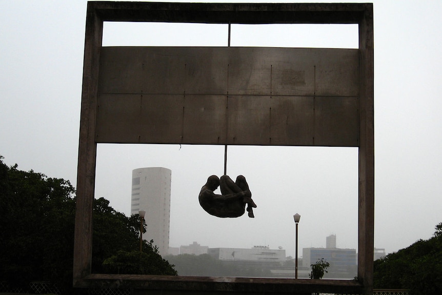 A stone sculpture of a curled man hanging from an arch commemorating the victims of Torture under Brazil's military dictatorship