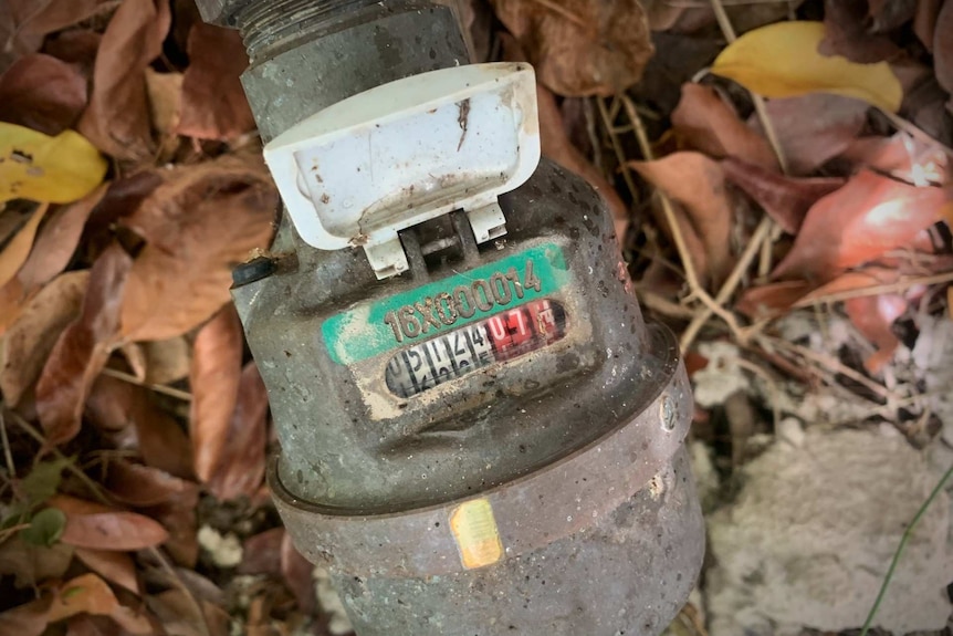 Top view of the digit tally counter of an old-style analogue water meter. Leaves on the ground.