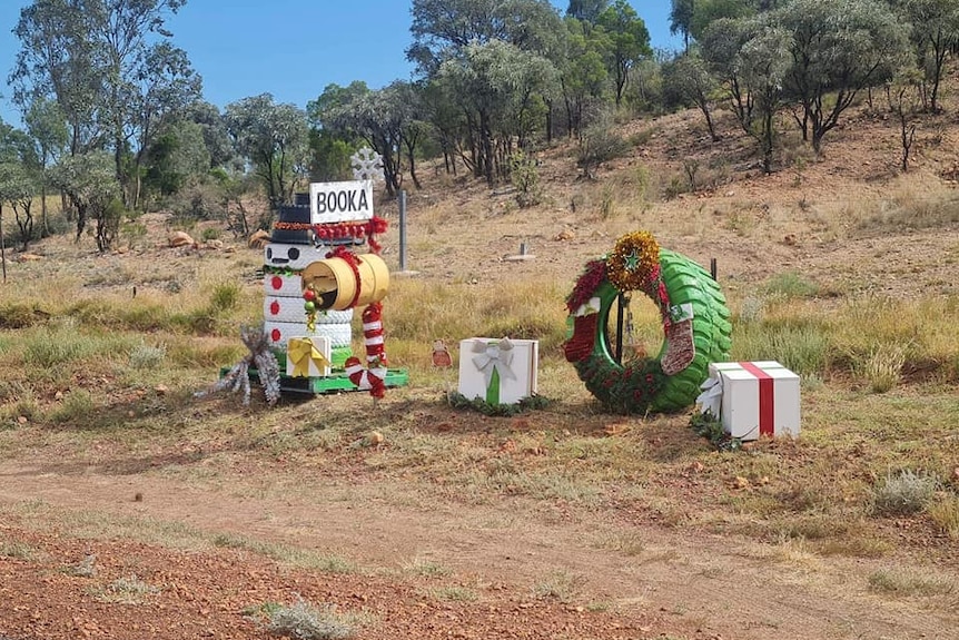 A mail box is surrounded by a snowman painted on tyres with a large tyre decorated as a wreath and presents