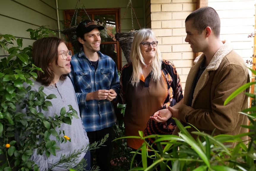 Four people stand are laughing in a backyard with many plants around them